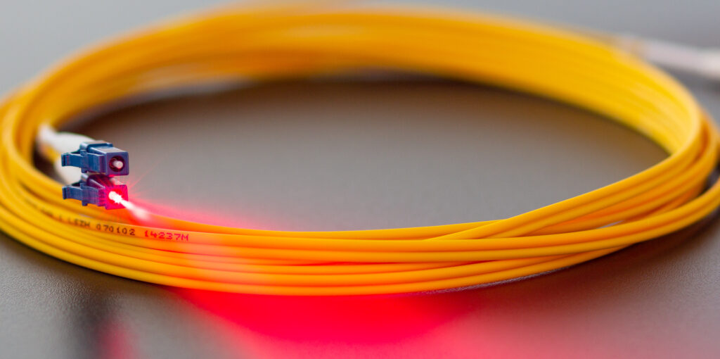Bild eines Glasfaserkabels mit beleuchtetem Stecker. Standleitungen über Glasfaser sind das Optimum